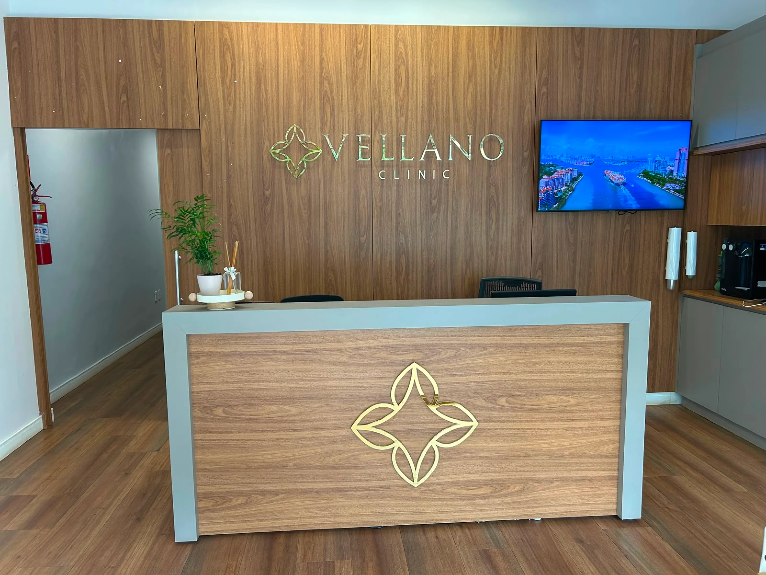Balcão de recepção da Vellano Clinic com painel de madeira e logo iluminada