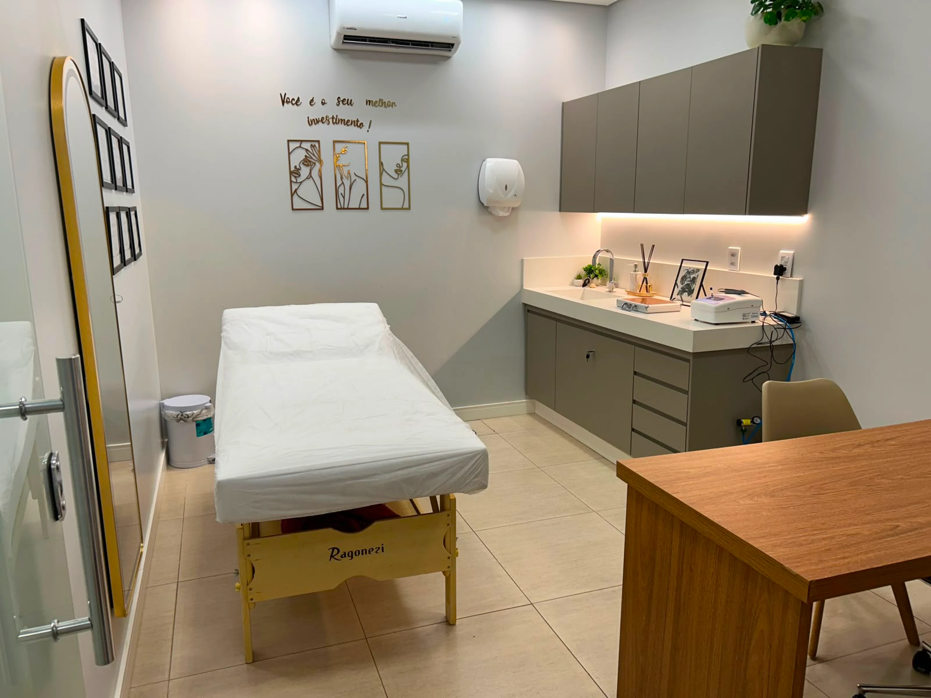 Sala de procedimentos estéticos com maca branca e bancada com armários